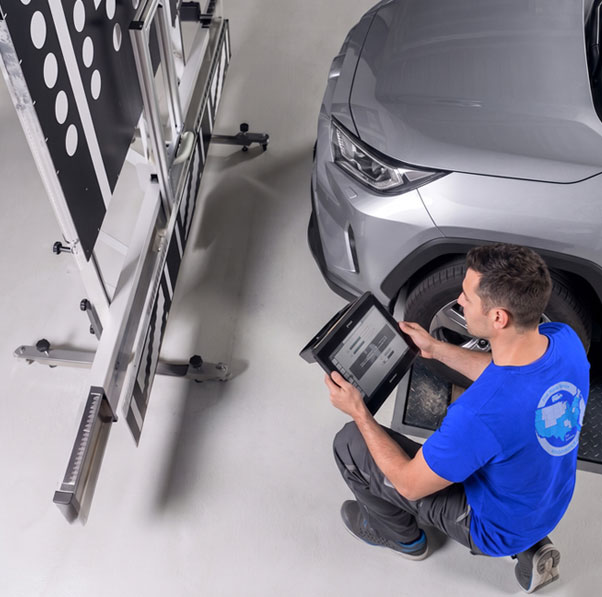 Technician setting up an ADAS calibration target frame beside a vehicle 