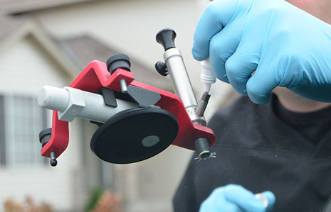 Technician using resin injection tool to repair windshield chip on-site