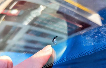 Finger pointing to a half-moon chip on a windshield before repair
